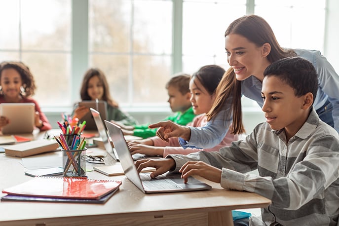 Young student looking at computer in classroom with teacher