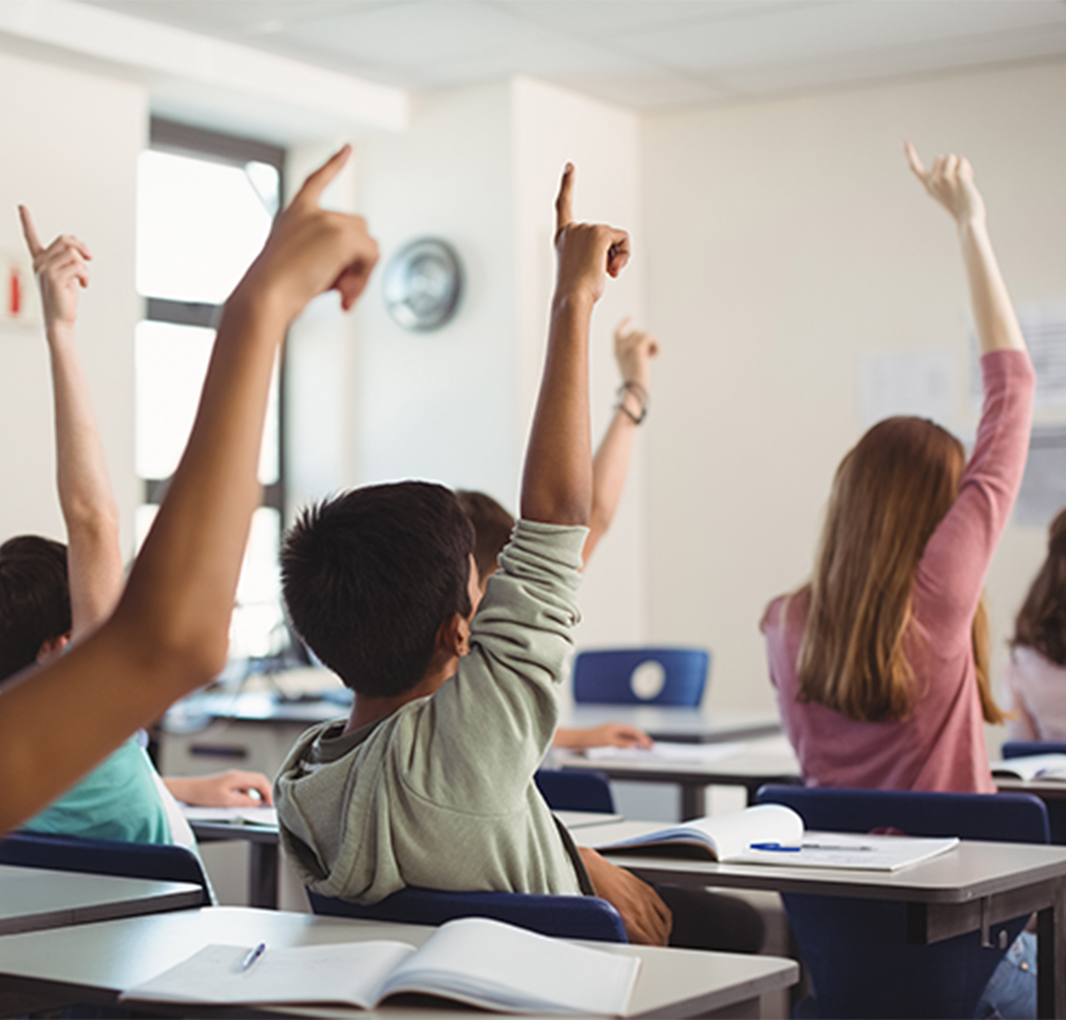 young students in classroom raising their hands