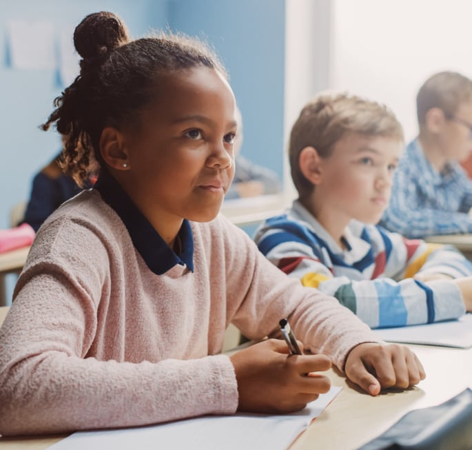 child in classroom learning and taking notes