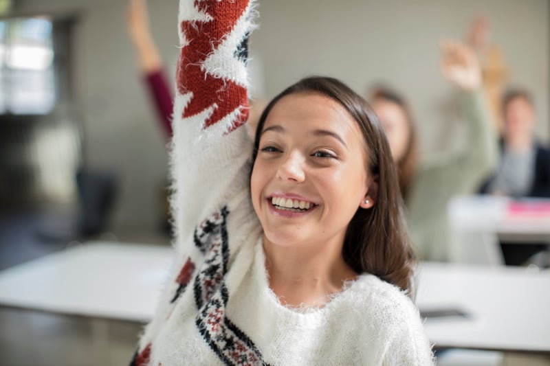 smiling teenage girl raising hand in class